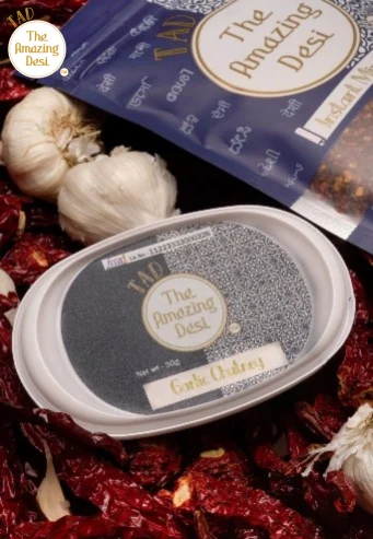 Close-up of TAD garlic chutney packaging surrounded by dry red chilies and fresh garlic bulbs.
